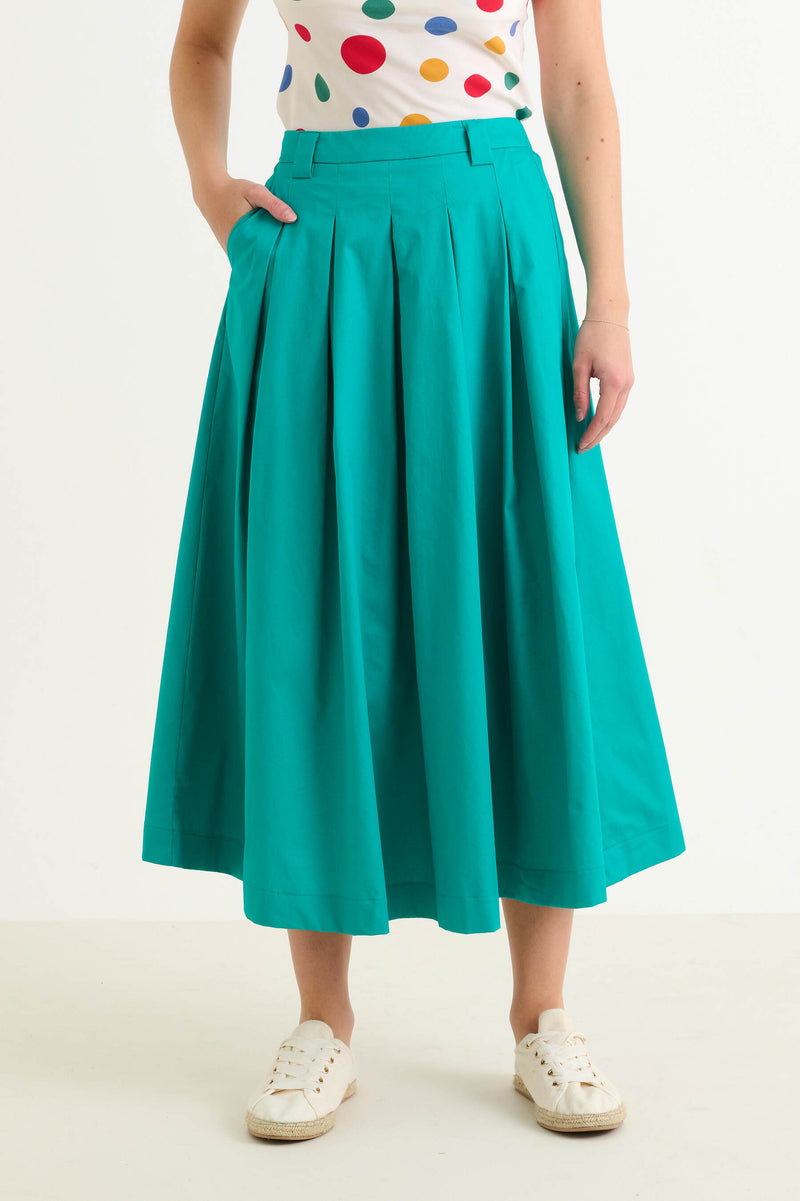 Person wearing a teal skirt and colorful polka dot top on a white background