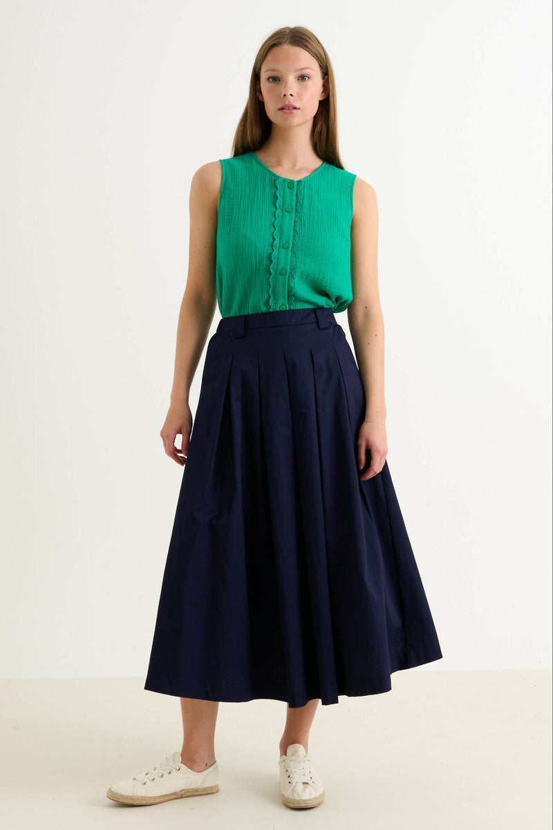 Woman wearing a green sleeveless top and navy skirt on a white background