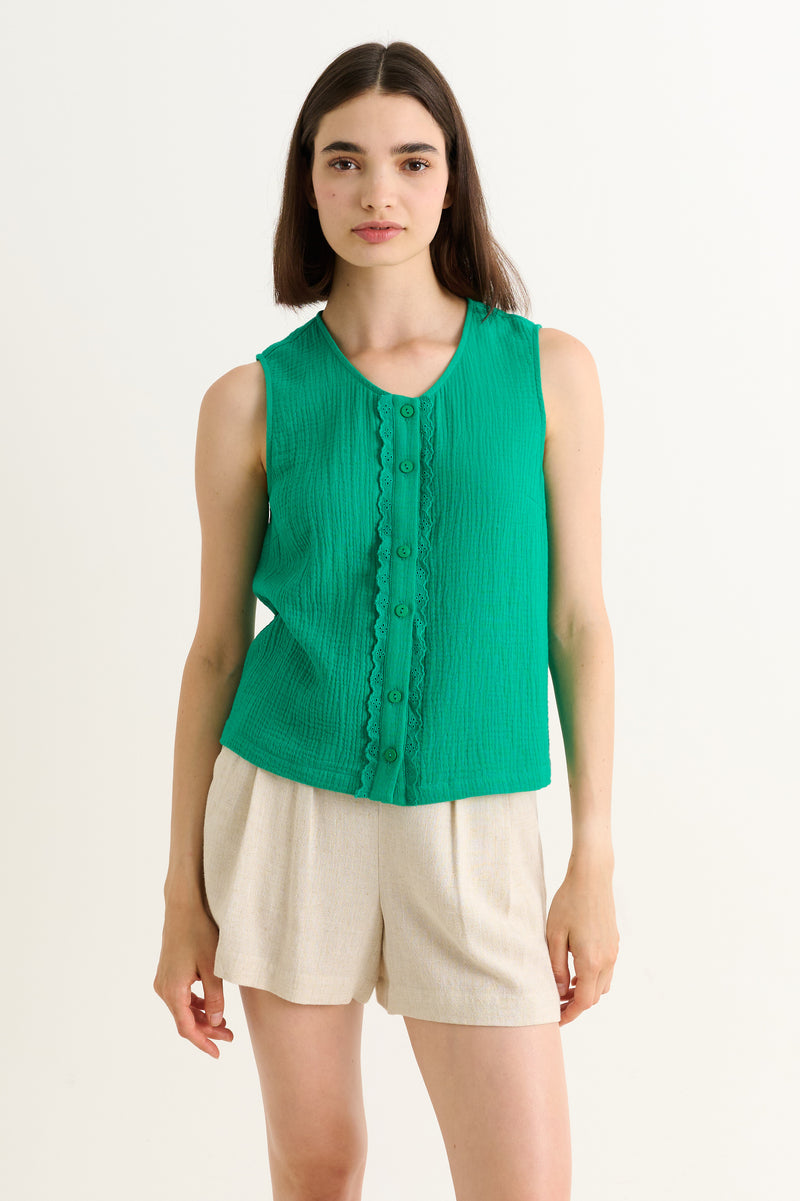 Woman wearing a green sleeveless top and beige shorts on a white background